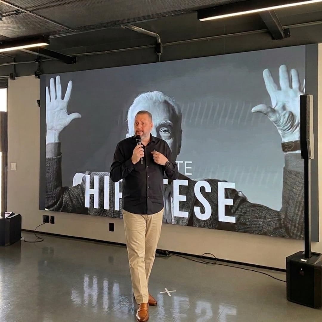 Luciano Passaretti palestrando em evento, com telão ao fundo