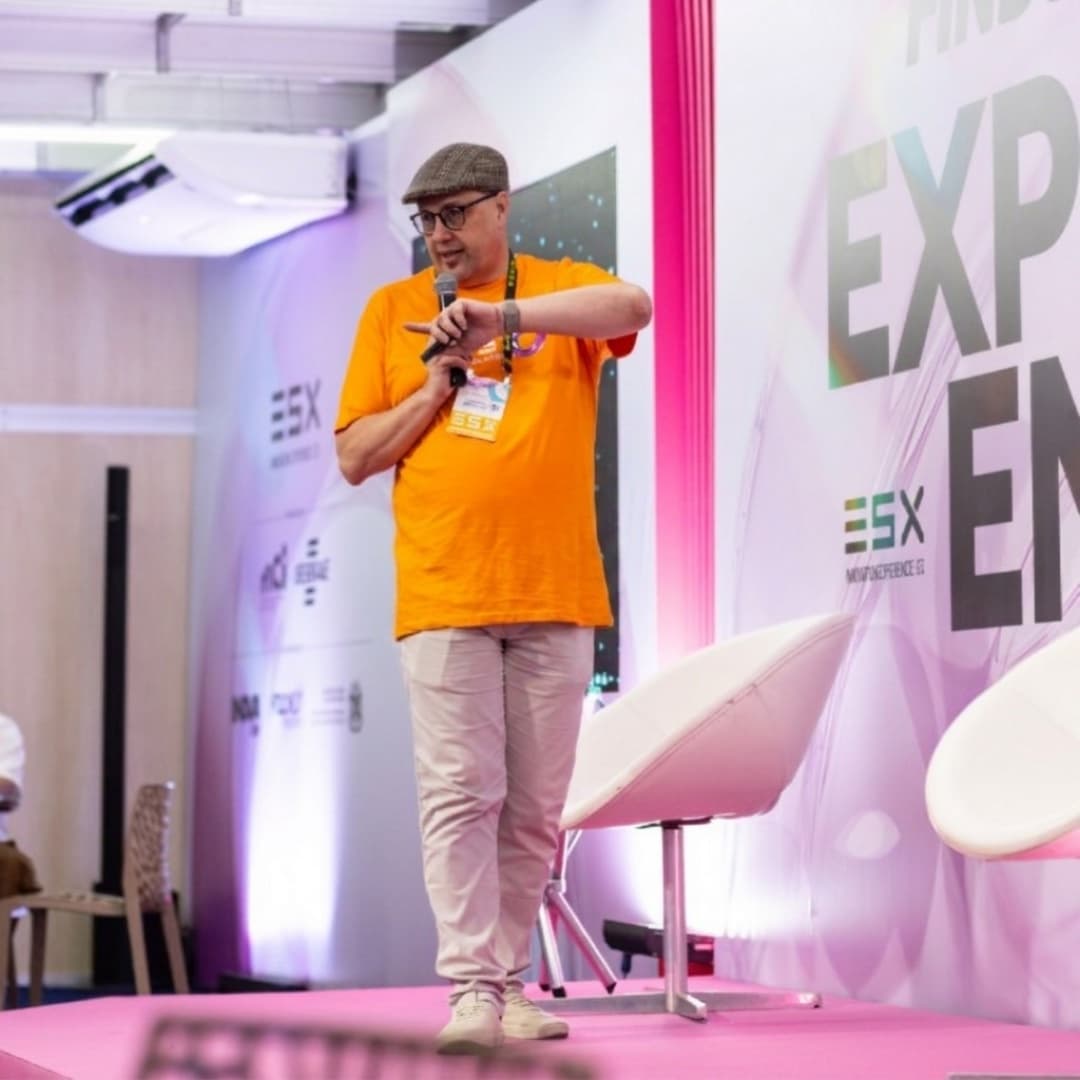 Luciano Passaretti palestrando no palco do evento ESX, vestindo camiseta laranja